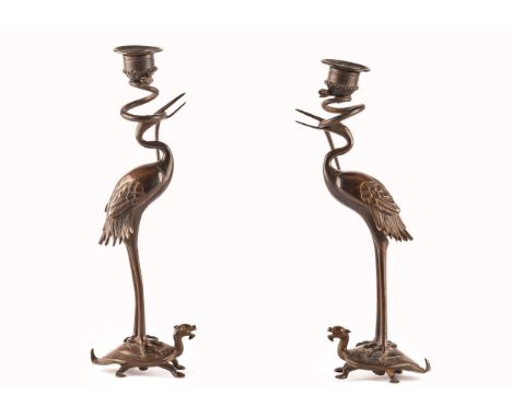 A pair of Japanese Meiji period bronze candlesticks, each in the form of a crane standing on the back of a turtle with a serp