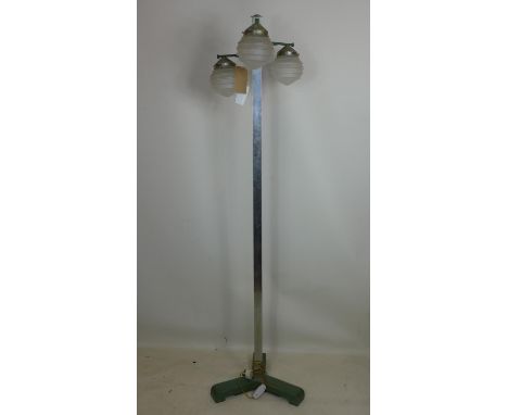 An Art Deco cast metal floor standing lamp, with three branches having stepped domed glass shades, on tri-form green painted 
