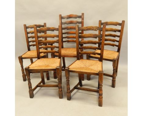 A set of five distressed oak ladder back chairs in the manner of Titchmarsh and Goodwin, each with a rush seat, one with arms