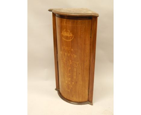 A small Edwardian mahogany bow fronted hanging corner cabinet, the top with a moulded edge, above a single door, inlaid with 