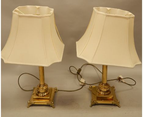 A pair of modern brass lamp bases, each with paw feet and a cream shade, the bases, 67cm high. 