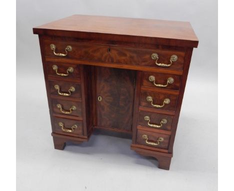 A figured mahogany and kneehole desk, with a frieze drawer above an arrangement of eight drawers around a kneehole with a cup