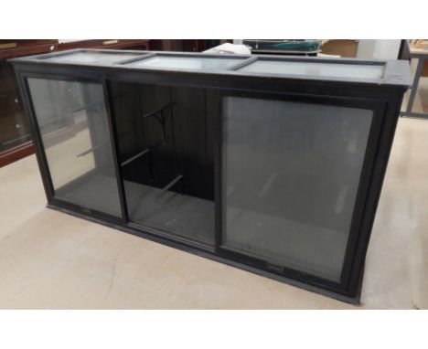 An ebonised shop display cabinet, with a glazed top, sides and two sliding drawers to the front, enclosing various shelf brac