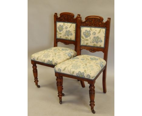 A pair of late Victorian walnut side chairs, each with a carved back, a padded seat, on turned tapering legs, with ceramic ca