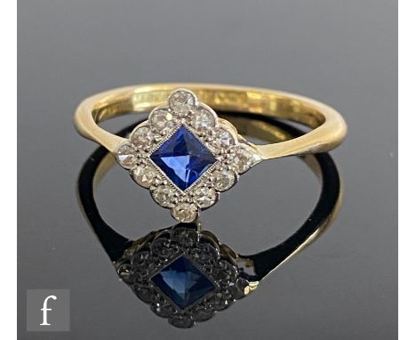 An early 20th Century 18ct sapphire and diamond cluster ring, central off set square sapphire within a twelve stone diamond b