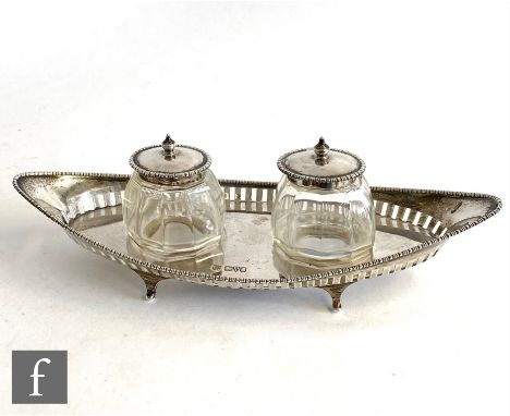 A hallmarked silver desk set of elongated oval form with raised pierced gallery supporting twin glass wells with silver hinge