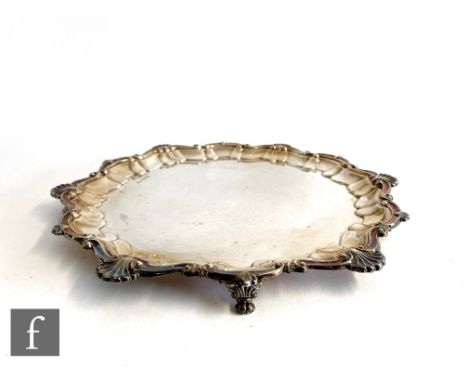 A hallmarked silver circular salver of plain form with scallop and shell border, raised on three feet, weight 26.5oz, Sheffie