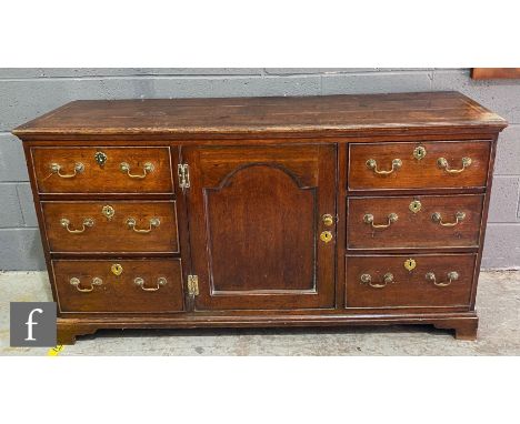 A small George III oak dresser base enclosed by a recessed central arch cupboard door flanked by three short drawers to each 