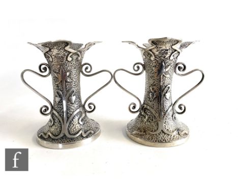 A pair of hallmarked silver Art Nouveau small twin handled vases, each decorated with stylised flowers to a beaten ground and