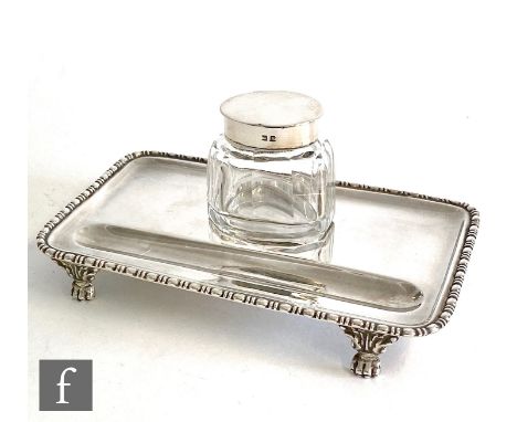 A hallmarked silver desk stand of rectangular plain form with egg and dart border supporting a single glass well with silver 