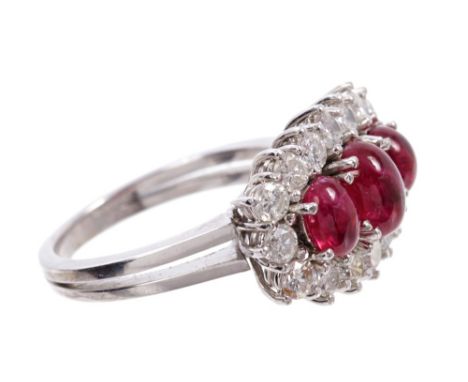 Ruby and diamond cocktail ring with three oval cabochon rubies surrounded by a border of sixteen brilliant cut diamonds in cl