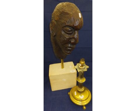 A carved wooden head ornament on a brass mount to stone plinth base, and a brass column table lamp