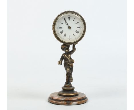 A brass pedestal cylinder desk clock. With enamel dial having Arabic and Roman markers, the central pedestal is formed as a p