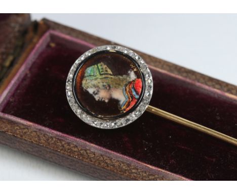 A cased yellow metal stick pin. Set with a Limoges enamel roundel portrait of a Medieval woman, monogrammed A. M. and under a