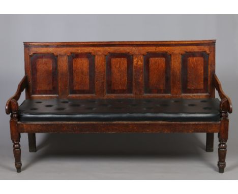 A George III oak panel back settle. With mahogany crossbanding, flat scrolling arms and raised on turned supports, 183cm wide