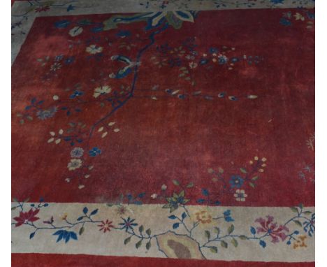 A Chinese red ground carpet circa 1930 having a bird resting on a branch with blossom within an ivory border, 270cm x 350cm