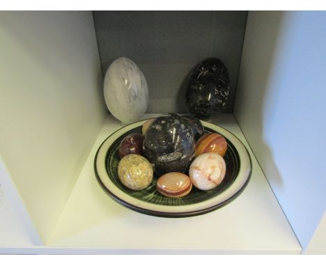 A ceramic shallow form bowl containing various polished stone eggs of various sizes