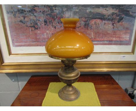 A brass oil lamp with an opaque glass amber shade