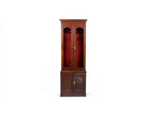 A late Victorian mahogany gun cabinet, the dentil cornice above a pair of tall glazed doors, opening to reveal an interior fi