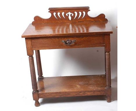 In the manner of Liberty &amp; Co - a circa 1900 oak single drawer ledgeback two-tier side table, the shaped and stylised pie