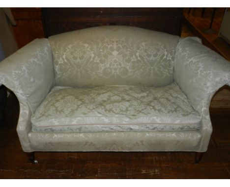 A 20th century camel back sofa, upholstered in a green floral fabric, raised on turned mahogany supports and casters. 