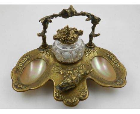 A brass inkwell, decorated with flowers and a duck, having mother of pearl wells and cut glass ink pot with lid in form of a 