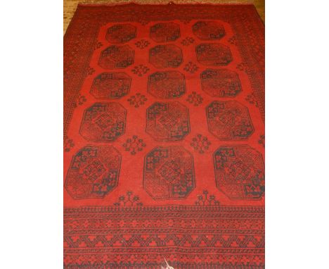 An red ground Afghan carpet, having three rows of elephant pad medallions to centre, within reticulated borders, fringed. L.2
