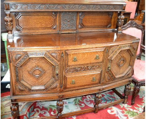 A Jacobean Revival oak sideboard, substantial half-gallery carved and applied with fruiting vine, flanked by two urnular pill