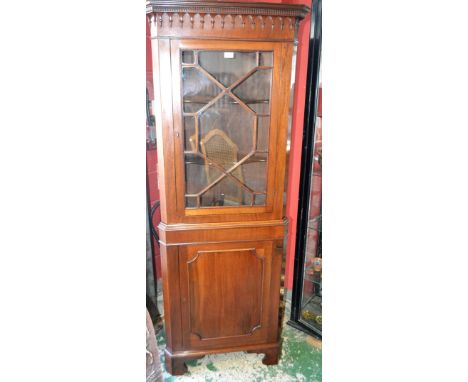 An early 20th century mahogany floor standing corner display cabinet, outswept dentil cornice above a glazed door enclosing t