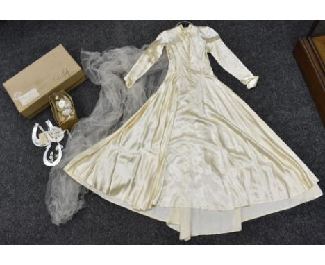 A mid 20th Century wedding dress, cream satin, button front, bias cut skirt with fine net veil, wedding accessories