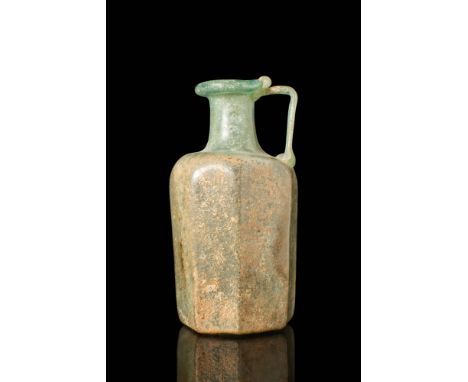 Ca. AD 100 - 300 .
A glass bottle with a large polygonal section body, a short narrow neck, and a folded rim. A strap handle 