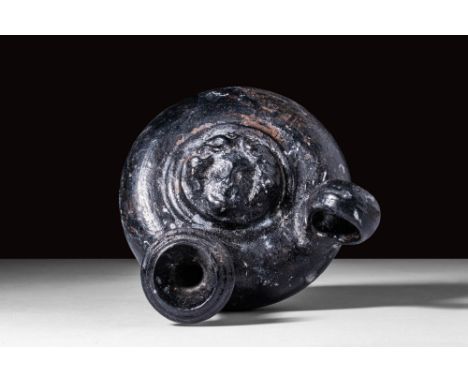 Ca. 350 - 300 BC.
A black-glazed pottery guttus bearing the feminine face of a gorgon atop the tondo, perhaps representative 