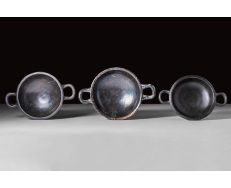 Ca. 400 - 300 BC.
A collection of three black glaze kylikes, each with a shallow body flanked by two horizontal handles and a