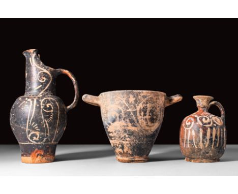 Ca. 450 - 350 BC.
A set of three terracotta black glaze vessels. The first is an oinochoe with a diagonal spout adorned with 