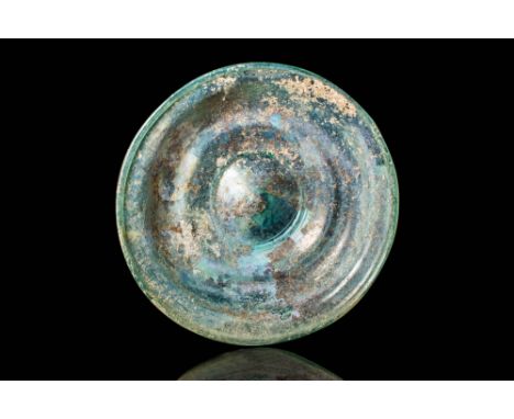 Ca. AD 100 - 300 .
A shallow glass mesomphalos bowl in colourless glass with a pale blue-green tinge. It features a rounded r