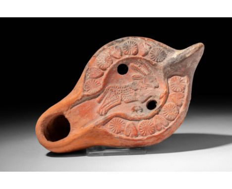 Ca. AD 400 - 500 .
A terracotta oil lamp presenting a recessed tondo with the relief image of a leaping horned stag. The elon