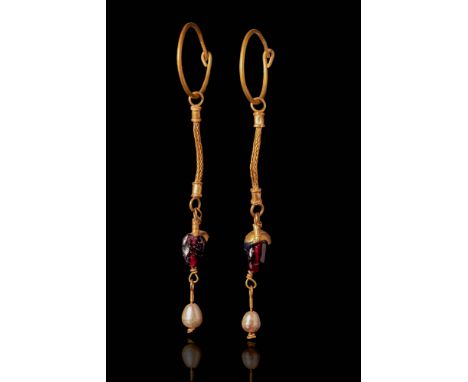 Ca. 600 BC.
A matching pair of gold earrings, each with a tapering hoop, hook-and-clasp closure, and a single elongated penda