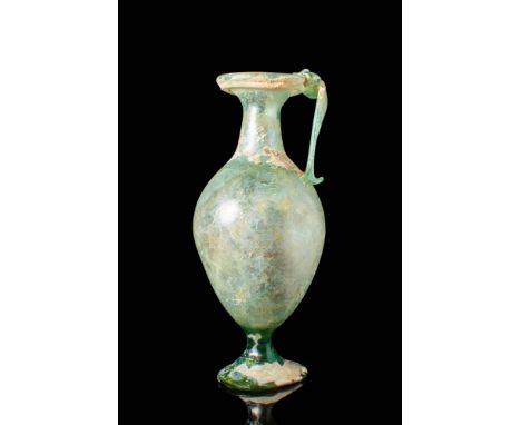 Ca. AD 100 - 300 .
A glass jug with an inverted pear-shaped body seated on a high pedestal, a short narrow neck connected to 