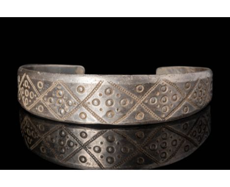 Ca. AD 900.
A silver penannular bracelet with a flat-section hoop engraved with geometric motifs comprising lozenges and dots