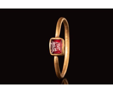 Ca. AD 400 - 600.A gold ring with a flat-section round hoop connected to a square bezel securing a red garnet intaglio depict