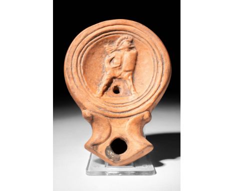 Ca. AD 40 - 100.
A pottery oil lamp presenting a recessed tondo with the relief image of a fighting gladiator wearing a high 