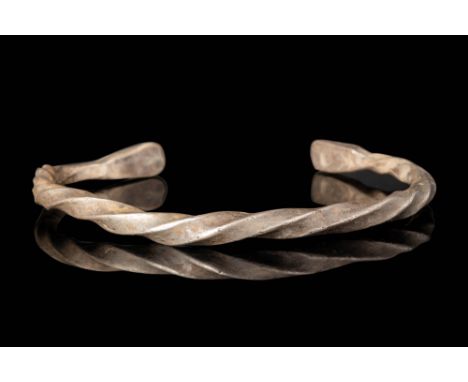 Ca. AD 900.
A silver bracelet with a twisted section hoop engraved with flat polygonal finials. A brown patina developed in s