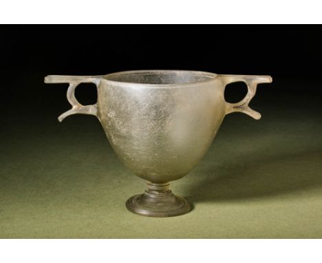 Ca. Late 3rd century BC.
A colourless cast glass skyphos with a deep, tapered body supported by a short stem with wheel-cut b