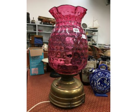 A brass oil lamp with massive cranberry glass shade (converted to electricity).