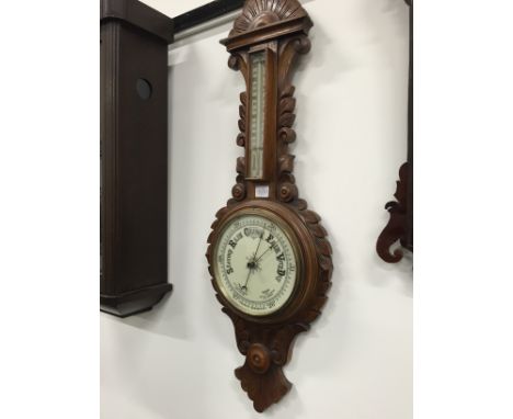 An early 20th century carved oak cased aneroid barometer and thermometer.
