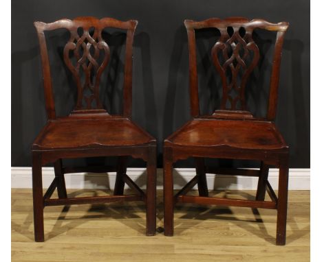 A pair of George III red walnut/mahogany hall chairs, each with Cupid’s bow cresting rail above a pierced Chippendale design 