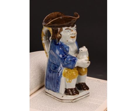 An early 19th century Prattware Toby jug, seated holding a jug of foaming ale, painted in polychrome in tones of yellow, blue