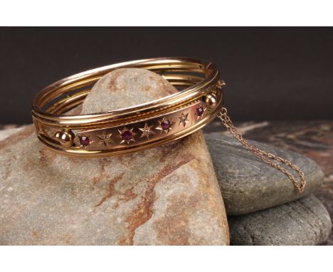 An Edwardian ruby and diamond 9ct gold hinge bangle, set with four old cut pinky red rubies, each divided by a rose cut diamo