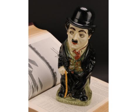 A Royal Doulton jug and cover, modelled as Charlie Chaplin, he stands wearing baggy black suit with cane in hand, the cover a