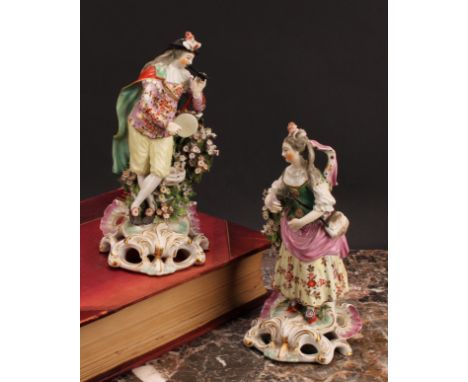 A Derby pair of patch mark figures, of Musicians, she stands playing the triangle, wearing feathers in her hair, floral skirt